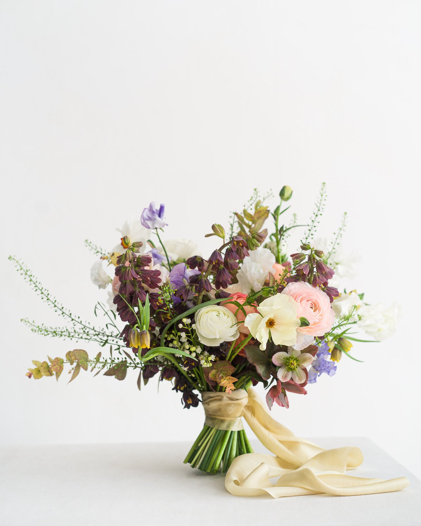 Beautiful spring Bridal Bouquet featuring delicate spring flowers including narcissus flowers, sweetpeas, fritillaria, ranunculus and hellebore from Aspen Florals Wedding Collection
