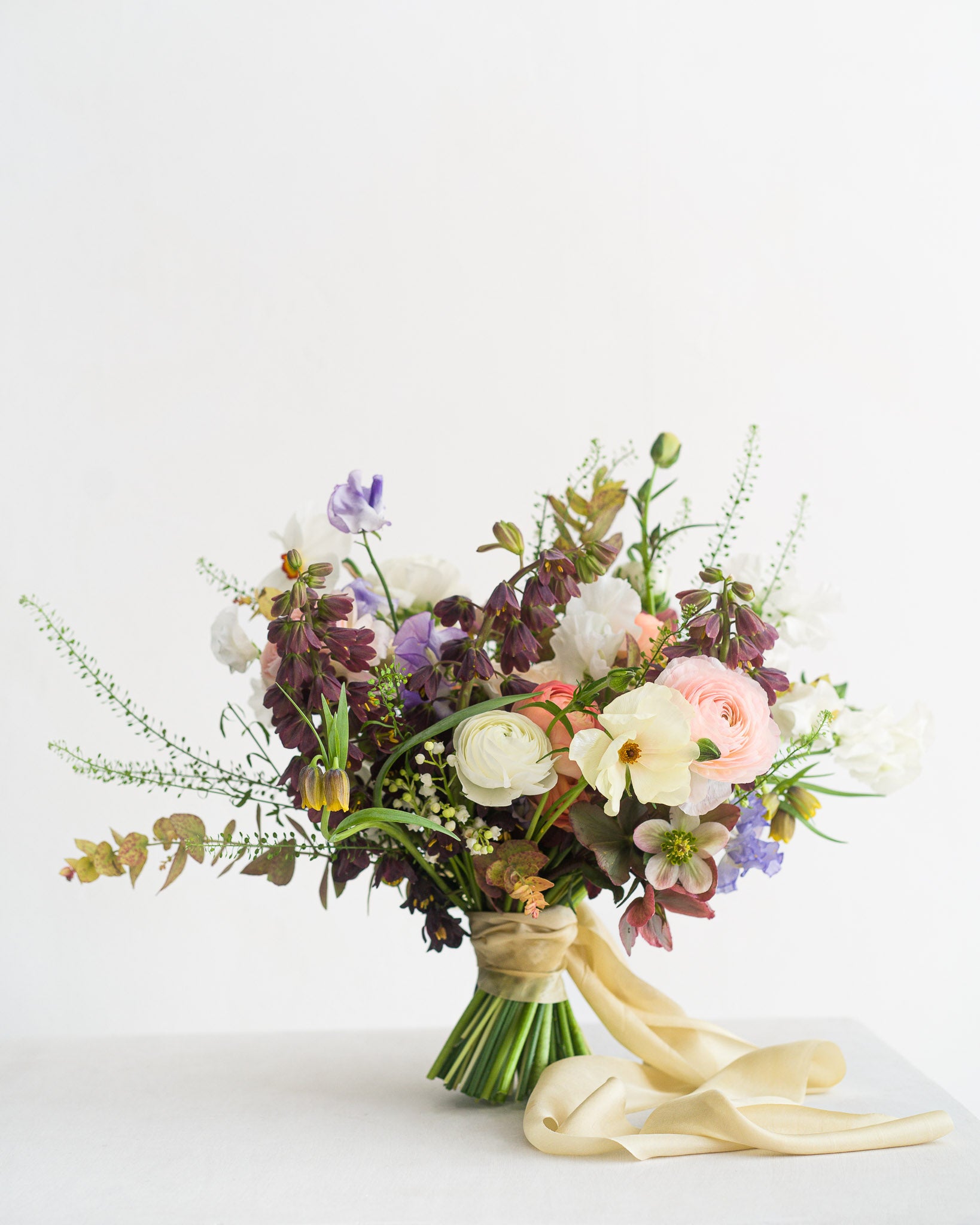 Beautiful spring Bridal Bouquet featuring delicate spring flowers including narcissus flowers, sweetpeas, fritillaria, ranunculus and hellebore from Aspen Florals Wedding Collection